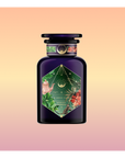 Moonlight in Marrakesh: Spiced Mint Green Tea comes in a dark purple bottle with a green and floral label, gold accents, and botanical art, evoking Moroccan mint tea against a soft peach and pink gradient backdrop.
