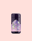 A purple cylindrical container labeled “Perfumes of Provence: Lavender Bouquet Tea for Calm Moods and Beautiful Skin” features pastel florals and geometric designs, standing out against a light pink background.