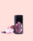 A black cylindrical container of “Breakfast in Paris-Oolong Black Tea Scented with Fruits & Flowers of Secret Parisian Gardens” stands on a pale pink background, adorned with petals and an orchid—suggesting the romance of Parisian gardens.
