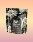 A black floral-patterned packet labeled "Goddess of Earl: Madagascar Vanilla Creme Tea for Soothing Delight & Delicious Decadence" sits centered on a soft peach-to-pink gradient background.