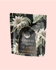 A stand-up pouch of Goddess of Earl: Madagascar Vanilla Creme Tea for Soothing Delight & Delicious Decadence features a dark floral design with white flowers, green leaves, and a light pink label. This blend includes organic black tea and bergamot vanilla.