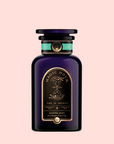A dark purple glass jar labeled "Magic Hour" with gold and green accents, hourglass and celestial designs. Label reads "Time for Infinity" and "Mantra Mint™ Herbal Tea," an ashwagandha-infused, caffeine-free blend on a light pink background.