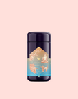 A dark purple cylindrical container with a reflective finish, labeled with mystical imagery and blue accents, hints at probiotic-rich Thai Temple Tea Puerh, set against a pale pink background.