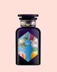 A dark purple glass bottle with a black cap and a colorful label showing figs, lemons, flowers, and leaves on light pink. The label reads "Summer in Amalfi"—a Mediterranean tea with organic herbal tea notes.