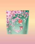 A floral green tea package named "Queen of Kyoto," featuring Japanese Cherry Blossoms and hummingbirds on a pastel gradient, highlights premium Sencha Green Tea.