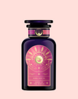 A dark purple glass bottle with a decorative label showing a golden sun, leaves, and pink accents. Labeled “Queen of the Tropics: Rosé all Day Alternative Tea,” it features Garcinia Cambogia and tropical fruits as a non-alcoholic rosé option. Light pink background.
