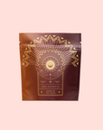 The "Queen of the South Cocoa Detox Tea" comes in a brown pouch with gold geometric sunburst designs and text on a pale pink background, offering an organic, soothing, caffeine-free herbal tea option.