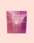 A pink and purple resealable pouch labeled "Queen of the Tropics: Rosé all Day Alternative Tea," with gold sun and leaf accents, presents this refreshing, energy-boosting tropical tea as a unique rosé wine alternative.