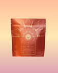 The "Queen of the Harvest: Herbal Relaxation Tea" bag features gold hands holding a radiant sun with celestial designs on a red and orange background, accented by a soft peach and pink gradient.