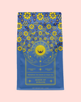 A blue tea package with ornate yellow floral and sunburst patterns reads “Queen of Ukraine: Spring Blossom Tea,” set against a pastel pink background.
