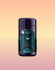 A dark purple cylindrical canister labeled "Aquamarine Dream - Soothing Herbal Ayurvedic Adrenal Tonic" with a teal and gold geometric design, featuring a calming blend, sits centered on a pastel peach, yellow, and pink gradient background.