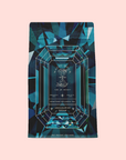 A blue and teal geometric tea package labeled "Aquamarine Dream - Soothing Herbal Ayurvedic Adrenal Tonic," a calming herbal tea with a gemstone illustration, is displayed against a light pink background.