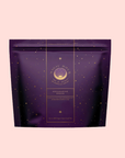 A purple resealable tea pouch labeled “Aquamarine Dream - Soothing Herbal Ayurvedic Adrenal Tonic,” adorned with gold star patterns, sits against a light pink background.