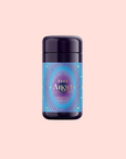 A dark purple container of 444: Sachiel's Prosperity Apple-Berry Herbal Tea with Butterfly Pea Flower and Blue Spirulina sits centered on a pale pink background, its blue and purple label adorned with gold and blue decorative designs.