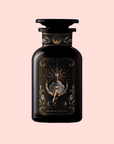 A dark glass bottle labeled "The High Priestess Ginger-Mint-Cardamom Tea Powerful Dreams & Illuminated Insights" features an illustrated crowned woman in a flowing dress on an ornate label, set against a light pink background with organic, caffeine-free ingredients.