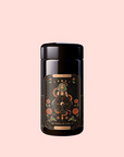 A dark jar with an ornate label displaying tarot card art, floral patterns, and "Magic Hour" with "The Wheel of Fortune: Ginseng Spice Tea for Adapting to Change"—a caffeine-free adaptogenic blend on a soft pink background.