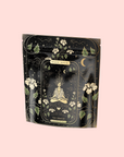A black and gold tea package with an illustrated meditating figure, celestial elements, flowers, moons, and stars. The front reads "Magic Hour," "The Oracle: Lemon Lavender Tea for Supporting the Gut-Brain Axis," and "adaptogenic tea blend.