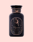 A dark glass perfume bottle labeled "Aquarius: Visionary Goddess Tea," adorned with gold art of a woman pouring water, stars, and flowers—evoking Yunnan black tea’s elegance—set on a light pink background with delicate details.