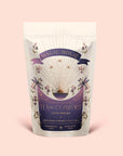 A pastel pouch labeled “Tea for Comfort: Lucid Dreams: Turmeric-Tulsi Chai Tea” features celestial and floral artwork, highlighting a soothing, caffeine-free blend of Tulsi and turmeric. This ceremonial herbal tea for sleep is “made with love” and sits gracefully on a soft pink background.