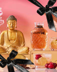 A golden Buddha statue sits beside pink flowers and luxurious tea drinks garnished with cherries, elegantly displayed on glass blocks. Black ribbons with gold text accent the scene, set against a vibrant pink and orange gradient background—creating The Best of Summer Poolside Sips Box, perfect for refreshing summer enjoyment.