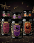 Three ornate black bottles with decorative labels—Haunted Hibiscus, Black Cat Brownie, and Candy Corn—stand against a dark, starry backdrop adorned with illustrated moths, dragonflies, and celestial motifs. This Halloween Bundle showcases limited edition hand-crafted tea blends from the Small Batch Magic Halloween Edition, perfect for celebrating the enchanting spirit of the season.