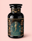 A black jar of Hathor of Joy: Honey Nectar Herbal Tea with gold and teal floral designs and an illustration of a goddess on the label, set against a light pink background. This caffeine-free herbal tea features soothing notes of blue lotus for a tranquil experience.