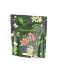 A green floral packaging of Hibiscus Elderberry: Cosmic Garden Iced Tea featuring organic hibiscus and elderberry. The front is adorned with illustrations of pink hibiscus flowers, elderberries, and various green leaves. The brand name "Magic Hour" is displayed at the bottom, highlighting their premium loose leaf tea collection.
