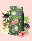 Certainly! Here’s a revised sentence using your product data: A package of Hibiscus Elderberry: Cosmic Garden Iced Tea is adorned with floral designs and surrounded by illustrated hibiscus flowers, elderberries, apple slices, and leaves on a pale pink background. This antioxidant iced tea blend delivers a refreshing burst of flavor and wellness in every sip.
