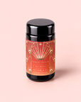 A black tea canister with a red and gold label reading “Hydrate Tea Boost” sits on a light pink background. The label, inspired by the vibrant energy of a botanical elixir, features geometric designs and a starburst motif.