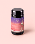 A black jar labeled “Kapha: Caffeine-Free Saffron Spice Tea” stands on a pale pink background. The purple and pink label features a silhouette of a stretching woman and emphasizes that this tea is designed for Ayurvedic digestion support and is caffeine-free.