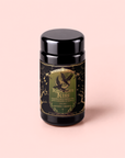 A black canister labeled “Kettle Corn Kiss: Sweet & Nutty Toasted Rice Green Tea with Caramel & Vanilla” features gold accents, an owl illustration, and ornate designs, set against a pale pink background.