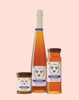 Three jars of Savannah Bee Co. Honey - Lavender sit against a light pink background, crafted by bilingual beekeepers inspired by Southern European traditions, each in varying sizes with white labels featuring lavender accents.