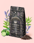 A decorative black tea bag labeled “Lavender London Fog Earl Grey Refill Pouch” is surrounded by lavender sprigs, bergamot fruit, and loose Earl Grey tea leaves on a soft pink background.