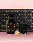 The Leo Astrology Tea Gift Set includes a black and gold starry box, a zodiac Leo jar, Opal Moon astrology tea, and a gold tea infuser—all shown on a pink gradient background.