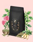 A package of "Libra Shatavari-Cardamom-Rose White Love Cake Tea" sits amid roses, green leaves, rose pistachio tea, a bowl of herbs, dried roots, and radishes on a pale pink background.