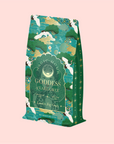 The elegant "London Fog Green" tea package showcases a decorative green and gold design with crane, cloud, and tree illustrations on a light pink background. The tea offers a fragrant allure with delicate notes of lavender intertwined with bergamot.
