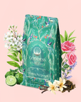 A green floral tea package labeled "London Fog Oolong" is surrounded by flowers, leaves, lime, and tea leaves, set against a light pink background. Infused with the delicate aroma of Quan Yin oolong and a hint of bergamot, this enchanting scene captures the essence of a truly unique blend.