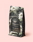 A standing organic black tea refill pouch labeled "Madagascar Vanilla Earl Grey Creme," adorned with white tropical flower illustrations and featuring notes of vanilla and cream, set against a light pink background.