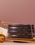 A Ceremonial Matcha Bowl features 14k gold star detailing, accompanied by a gold “Magic Hour” teaspoon, a tea infuser, a white rose, and a teabag, all arranged on a soft pink background.