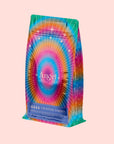 A colorful, rainbow-toned coffee bag with radiant starburst patterns and white stars. The front displays "777: Celestial Messengers Dawn," hinting at a sacred blend that inspires spiritual awareness with each sip.