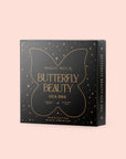 A black box with gold detailing and text on a light pink background. The box reads "Butterfly Beauty Gua Sha" with "Handcrafted Black Obsidian" at the bottom. The box, inspired by the elegance of Magic Hour, features a butterfly design and is decorated with small stars.