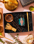 A Matcha 1111 : Gift Set containing a bamboo matcha whisk, powder canister, strainer, and scoop, arranged with a gold teapot, a bowl of prepared Japanese matcha tea, and a crystal candle holder.