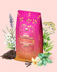 A vibrant tea package labeled "Mercury Mint Daytime : Vanilla Mint Lavender Jasmine Black Tea" is surrounded by herbs such as mint, lavender, vanilla, and chamomile, set against a pale pink background—hinting at a soothing blend inspired by vanilla mint and lavender jasmine flavors.