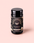 A black jar labeled “Metabolism Balance: Breakfast with Benefits” rests on a light pink surface, adorned with decorative gold and beige accents and suggesting a nourishing metabolism tea ideal for your morning ritual.