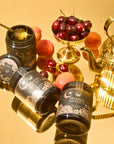 Jars of Moonflower 100% Raw, Antioxidant-Rich Wildflower Honey from Ojai, adorned with ornate labels, sit on a reflective gold surface. A golden teapot and a fruit stand enhance elegance, while a honey dipper hovers above the jars, highlighting this organic California treasure.