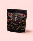 A luxury tea blend package, "Taurus: Tea of Venusian Garden Delights," features gold and red art—dancing woman, roses, sun rays, and crescent moon—on pale pink. Elegant antioxidant tea for those who cherish beauty and sophistication.