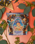 A vibrantly designed tea package labeled "Nuwa Tea for Intuition: Dragon Yuzu Oolong Case Packs" by Magic Hour is surrounded by eucalyptus leaves, flowers, and a star-shaped bowl of Organic Dragon Phoenix Jasmine Pearls. The background features a warm gradient of orange to red, creating an inviting atmosphere.