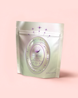 A silver, resealable pouch with a pastel magical design features stars and a round label reading "Pearl Tea of Beauty, Clarity, and a Sense of Peace" against a soft pink background.