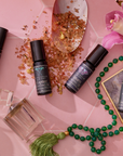The Planetary Perfume Bundle (Save $26 with the Bundle!), crystals, pink bath salts, a green beaded tassel necklace, and a pink orchid on a geometric surface evoke emotional balance and tranquility.