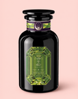 Set against a light pink background, the elegant Peridot: Green Guayusa Oolong Mango-Peach Tea comes in a black glass bottle adorned with a green, gem-shaped label and a decorative purple band near the cap. Inside, you’ll find an invigorating blend of organic guayusa and oolong tea infused with luscious mango and peach flavors.